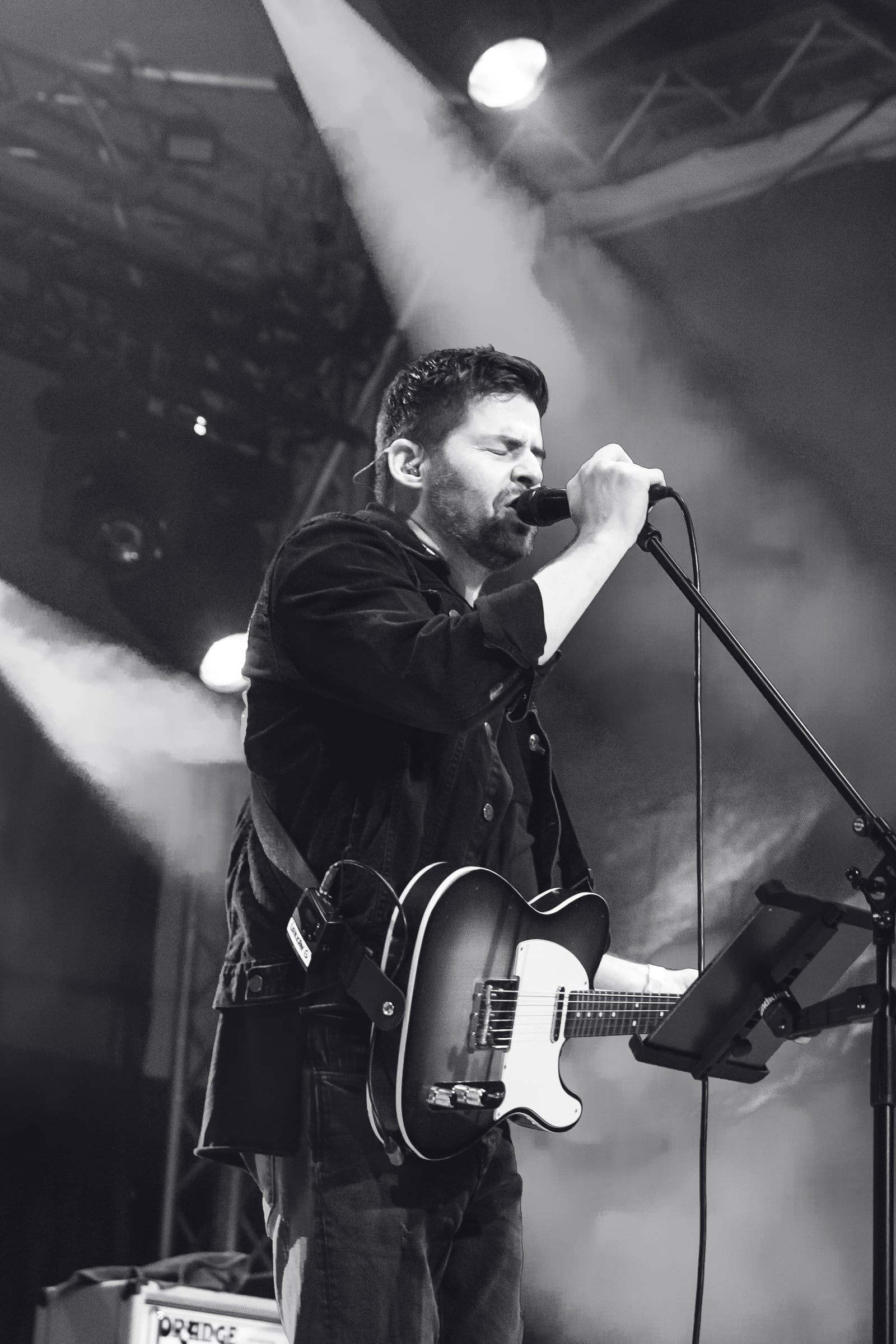 Spevák s gitarou pri mikrofóne, čiernobiela fotka na výšku